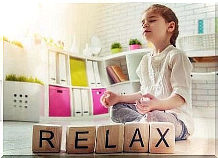 The word relax spelled out in wooden blocks with a child in meditation pose