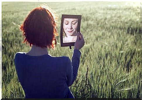 A woman stands in a field and looks in the mirror