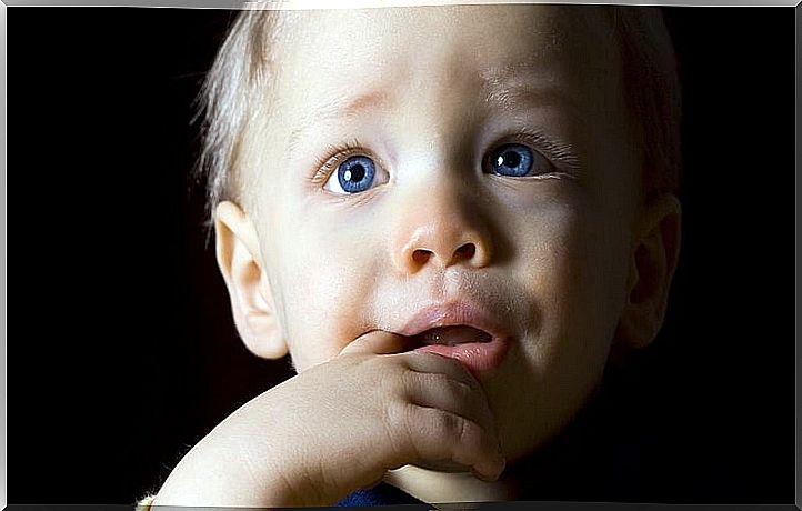 Little boy with blue eyes looking up with his finger in his mouth