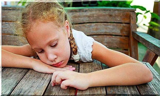 Girl hanging over a table aimlessly and unhappy as an example of childhood depression