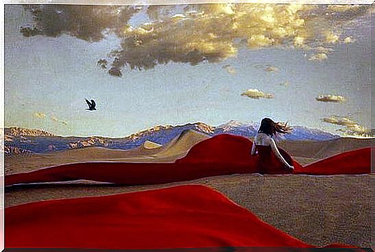 Woman in a red dress sitting alone in the desert to heal the emotional wound on her soul