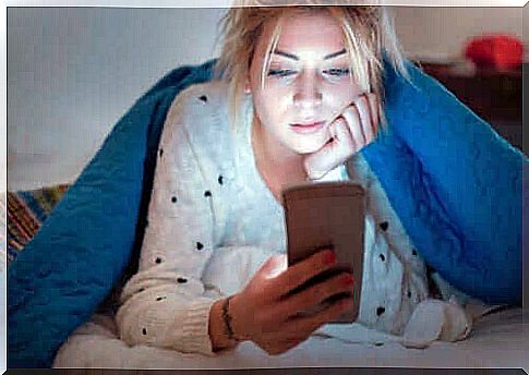 A woman looks at her cell phone in bed