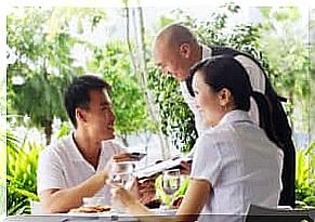 A smiling couple at the table gets the bill from a waiter