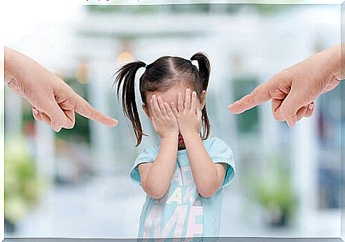 Girl standing with her hands over her eyes because two big fingers are pointing at her